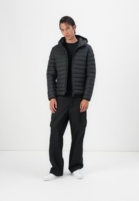 Sort pufferjakke med vandret syninger, frontlynlås og hætte, parret med løstsiddende sorte cargo-bukser og hvide sneakers.