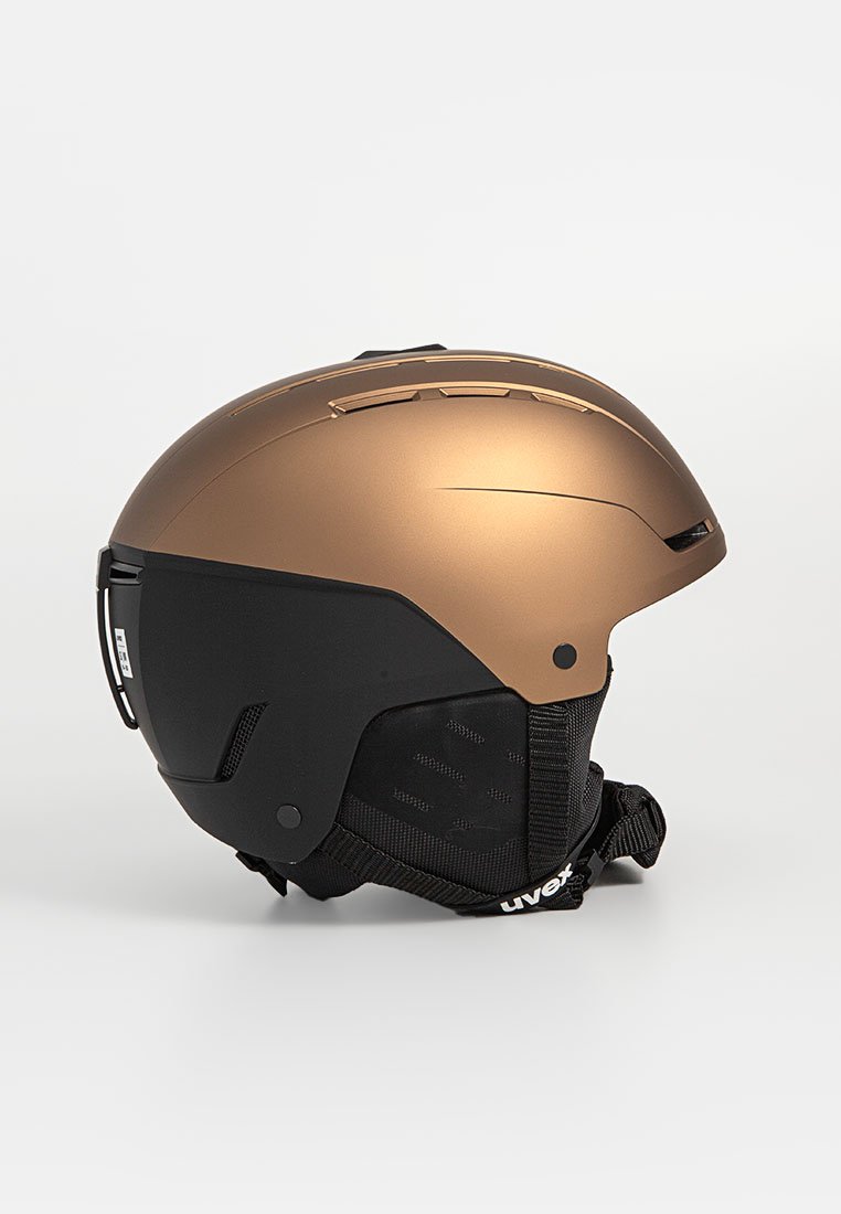 Kask narciarski z brązowym wierzchem, czarnym spodem, aerodynamicznym kształtem, otworami wentylacyjnymi i regulowanym paskiem pod brodą. Matowe wykończenie.