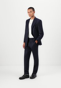 Marineblå stribet jakkesæt med dobbeltradet blazer, slim-fit bukser og en hvid t-shirt. Glat stof med sorte dress sko.
