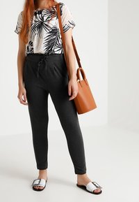 Svart och vit blommig kortärmad topp, grå avsmalnande byxor, brun handväska och svart och vit sandal med rem-detaljer.