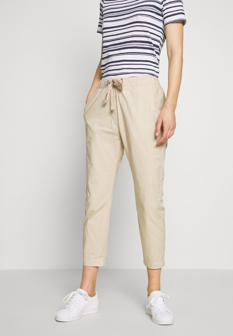 Pantalon beige léger et raccourci avec une taille élastique et un cordon de serrage; associé à un T-shirt rayé bleu marine et blanc et des baskets blanches.