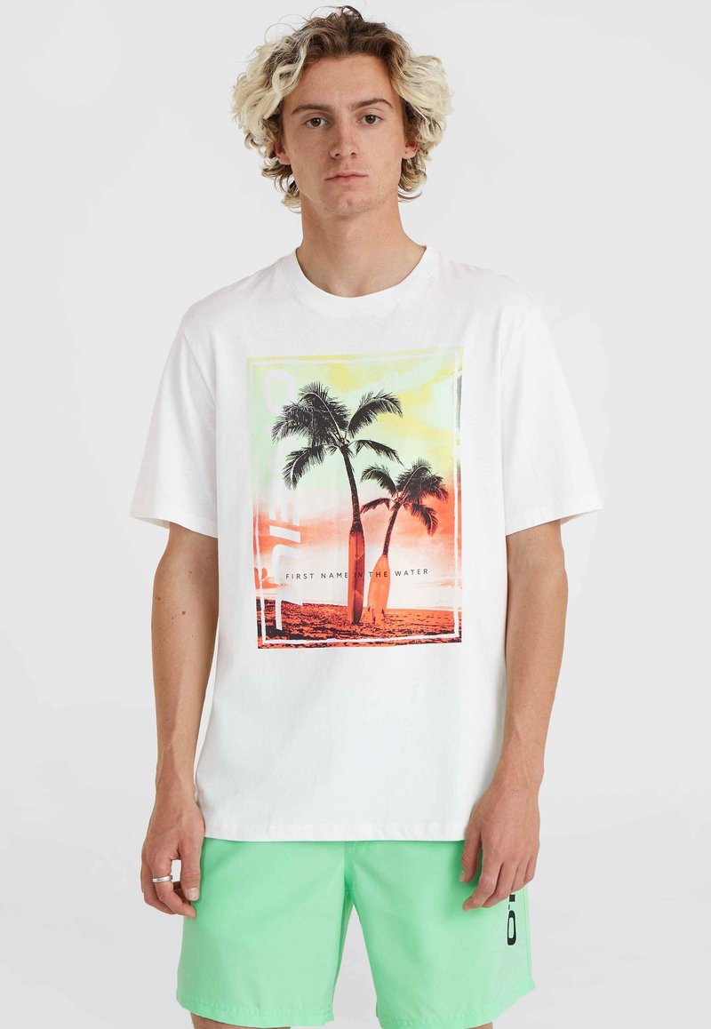 Camiseta blanca de algodón con un estampado gráfico de palmeras en tonos naranjas y verdes, con texto, combinada con pantalones cortos verdes claros.