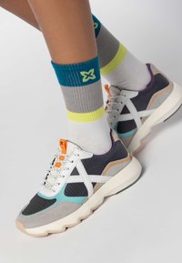 Le scarpe da ginnastica presentano un mix di materiali grigi, neri e acquamarina con accenti bianchi. Superfici testurizzate, dettagli arancioni e viola, e suole spesse.