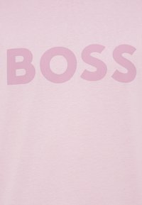 Gaiši rozā T-krekls ar izvirzītu, tumšāka rozā krāsā rakstītu vārdu "BOSS". Mīksta, gluda auduma ar ikdienišķu dizainu.