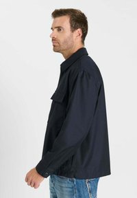 Marineblauw jack van gladde stof, voorzien van een kraag, borstzak aan de linkerkant en manchetten met knopen. Gestileerd met een ontspannen pasvorm en een rechte zoom.