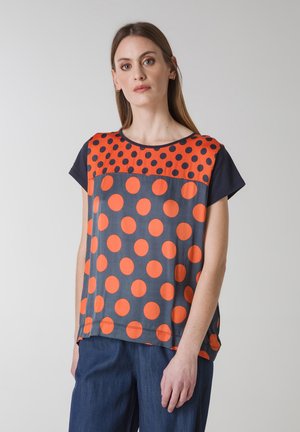 Kortærmet top med en marineblå bund, store orange prikker og en kontrasterende halsudskæring med orange og marineblå prikker.