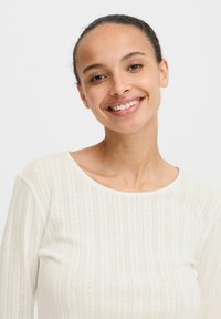 Witte long sleeve bovenstuk met een gestructureerd patroon van verticale strepen en kleine gaten, met een ronde halslijn. Gladde stofafwerking.