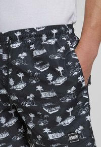 Fekete rövidnadrág fehér pálmafával és vintage autó mintával. Rugalmas derékrésszel és oldalsó zsebekkel rendelkezik. Könnyű anyagból készült.