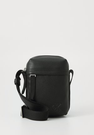Schwarze Leder Crossbody-Tasche mit strukturiertem Oberflächenmaterial, silbernem Reißverschluss, verstellbarem Tragegurt und eingeprägtem Logo auf der Vorderseite. Kompakte rechteckige Form.
