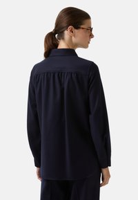 Marineblauwe blouse met lange mouwen en kraag, met een geplooide achterkant en een soepele textuur, ontworpen voor een ontspannen pasvorm.