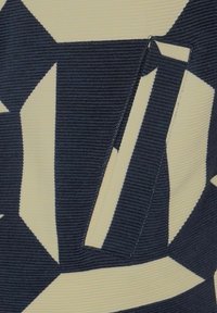 Vzorovaná tkanina s pravidelně se střídajícími tmavě modrými a krémovými geometrickými tvary, s ribbovanou strukturou a viditelným detailem kapsy po straně.