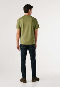 Olijfgroen katoenen T-shirt met korte mouwen, ronde halslijn en een relaxte pasvorm, gecombineerd met donkerblauwe jeans en een paar bruine enkellaarzen.