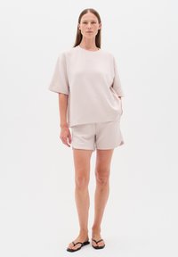 Světlý béžový top s krátkým rukávem a odpovídající šortky, vyrobené z měkké tkaniny. Má uvolněný střih a minimalistický design. Nosené s černými žabkami.