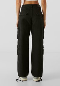 Pantalons cargo noirs avec une coupe ample, des poches latérales et des ourlets à cordon de serrage. Fabriqués en tissu durable avec une texture douce.