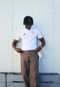 Hvit Adidas sportskjorte med røde detaljer, spansk landslagsemblem, paret med brune bukser. Enkelt design, atletisk passform.