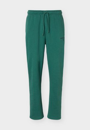 Grønne afslappede joggingbukser med elastisk taljebånd og snor, med lille sort logotekst på øverste venstre lår.
