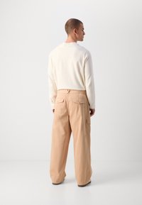 Beige cargo pants with a relaxed fit, featuring two back pockets, subtle stitching details, and a smooth, soft fabric finish.
