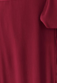 Červená textúrovaná tkanina s vertikálnymi záhybmi, mäkko splývajúca, s hladkým povrchom a jemným leskom. Žiadne viditeľné kovové prvky ani akcenty.