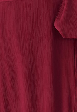 Tejido rojo texturizado con pliegues verticales, cayendo suavemente, con un acabado liso y un ligero brillo. Sin accesorios u ornamentación visibles.