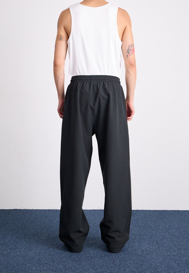 Černé, volné kalhoty s elastickým pasem, s hladkým povrchem a zúženým střihem nohavic. Nosené s bílým tílkem.