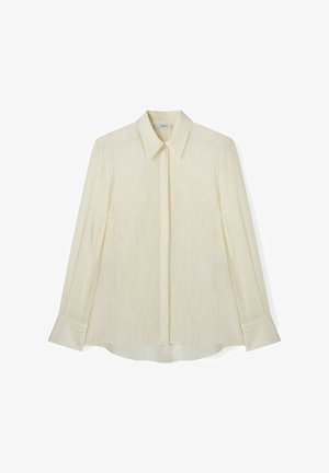 Bluza crem cu mâneci lungi, cu un model discret texturat, guler ascuțit, nasturi ascunși și manșete largi.