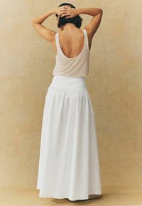 Jupe maxi blanche fluide avec taille froncée et texture lisse, associée à un haut en maille beige à dos plongeant.