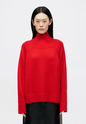Pullover in maglia rossa con colletto alto a coste e spalle scese. Presenta una vestibilità ampia e polsini e orlo a coste.