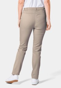 Beige, strakke broek met een gladde textuur en een elastische tailleband, gecombineerd met witte sneakers die een casual uitstraling van achteren benadrukken.
