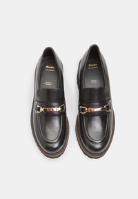 Mocassins en cuir noir avec un accent en chaîne dorée brillante, bout arrondi et semelle texturée. Comprend la marque "Bata Real Leather" à l'intérieur.