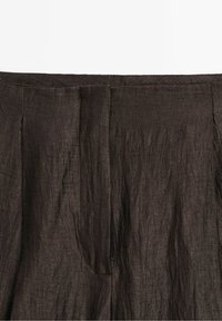 Gros plan d'un tissu en lin brun foncé avec texture visible et détails de plis, avec un focus sur une ceinture et une fermeture frontale cachée.