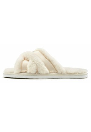 Faux fur slippers in cream color with double crossed straps and a soft, plush texture; white, flat rubber sole for indoor use.