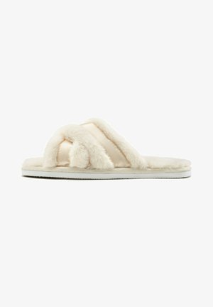 Faux fur slippers in cream color with double crossed straps and a soft, plush texture; white, flat rubber sole for indoor use.