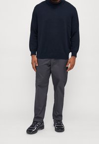 Pull en maille côtelée col roulé bleu marine, avec col et poignets côtelés, associé à un pantalon gris charbon et des baskets noires avec des touches violettes.