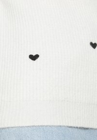 Tissu blanc texturé avec de petits motifs de cœurs noirs au-dessus d'un denim bleu clair.