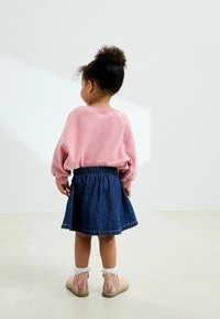 Sudadera rosa con mangas abullonadas, falda de mezclilla con cintura elástica y botas rosas con bordado de flores y un borde de encaje.