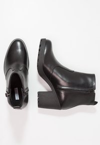 Bottes cheville en cuir noir avec talon épais, fermetures éclair latérales, bout rond, texture lisse et design minimaliste.