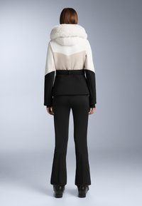 Tehnička skijaška jakna s kragnom od umjetnog krzna, s kolor blok dizajnom u bijeloj, bež i crnoj boji. Crne prilagođene hlače s proširenim rubovima.