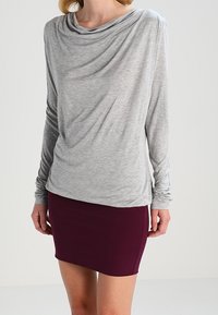 Maglietta grigia a maniche lunghe con collo drappeggiato, abbinata a una mini gonna fitted color bordeaux. Tessuto liscio, design casual e silhouette aderente.