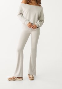 Sweatshirt léger beige à épaules dénudées associé à un pantalon de survêtement ajusté et évasé de la même couleur et des chaussures de sport avec des accents marron.