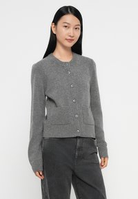 Cardigan gris avec un col rond, des poignets côtelés et deux poches à l'avant. Présente une fermeture à boutons et des détails en tricot texturé.