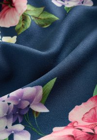 Cvetlična tkanina z rožnatimi in sivkastimi cvetovi na temno modrem ozadju. Gladek tekstura z nežnim sijajem in tekočim zavesanjem.