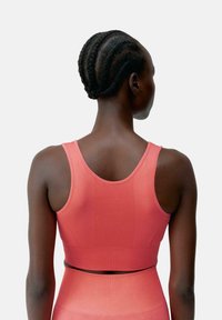 Rebrasta sports bra u koraljno roza boji s širokim naramenicama i prilagođenim dizajnom. Glatka tekstura i bešavni stražnji dio za udobnost tijekom vježbanja.