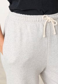 Svetlosivé teplákové nohavice vyrobené z mäkkej bavlnenej zmesi, s elastickým pásom, šnúrkou a bočnými vreckami.