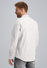 Camicia bianca a maniche lunghe con colletto a punta, polsini con bottoni e orlo dritto. Il tessuto appare tessurizzato e informale.