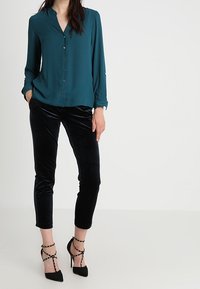 Teal knappad blus med v-ringning, långa ärmar och svarta sammet cropade byxor. Bärs med svarta högklackade skor med remmar.