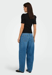 Top corto a maniche corte nero a coste abbinato a jeans in denim blu larghi. Il top ha maniche a palloncino; i jeans presentano tasche e una vestibilità comoda.