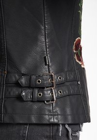 Czarna skórzana kamizelka z kwiatowym haftem, dopasowany krój oraz dwa zapięcia na klamry w talii z metalowymi detalami.