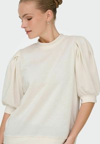 Cream-colored pullover sweater with puff sleeves, ribbed crew neckline, and soft texture. Features subtle sheen and relaxed fit.