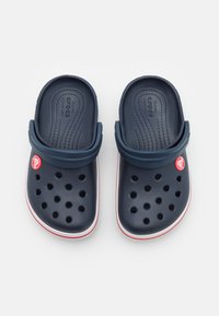 Zoccoli blu navy con design moldato, fori di ventilazione e bordo bianco e rosso. Presentano una fascia posteriore regolabile e un'applicazione del logo.
