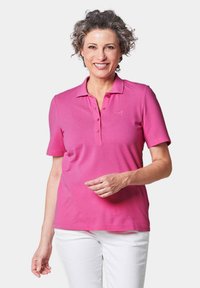 Rosa Poloshirt aus weichem Stoff, mit einem Knopfverschluss und kurzen Ärmeln. Logo auf der linken Brust gestickt.